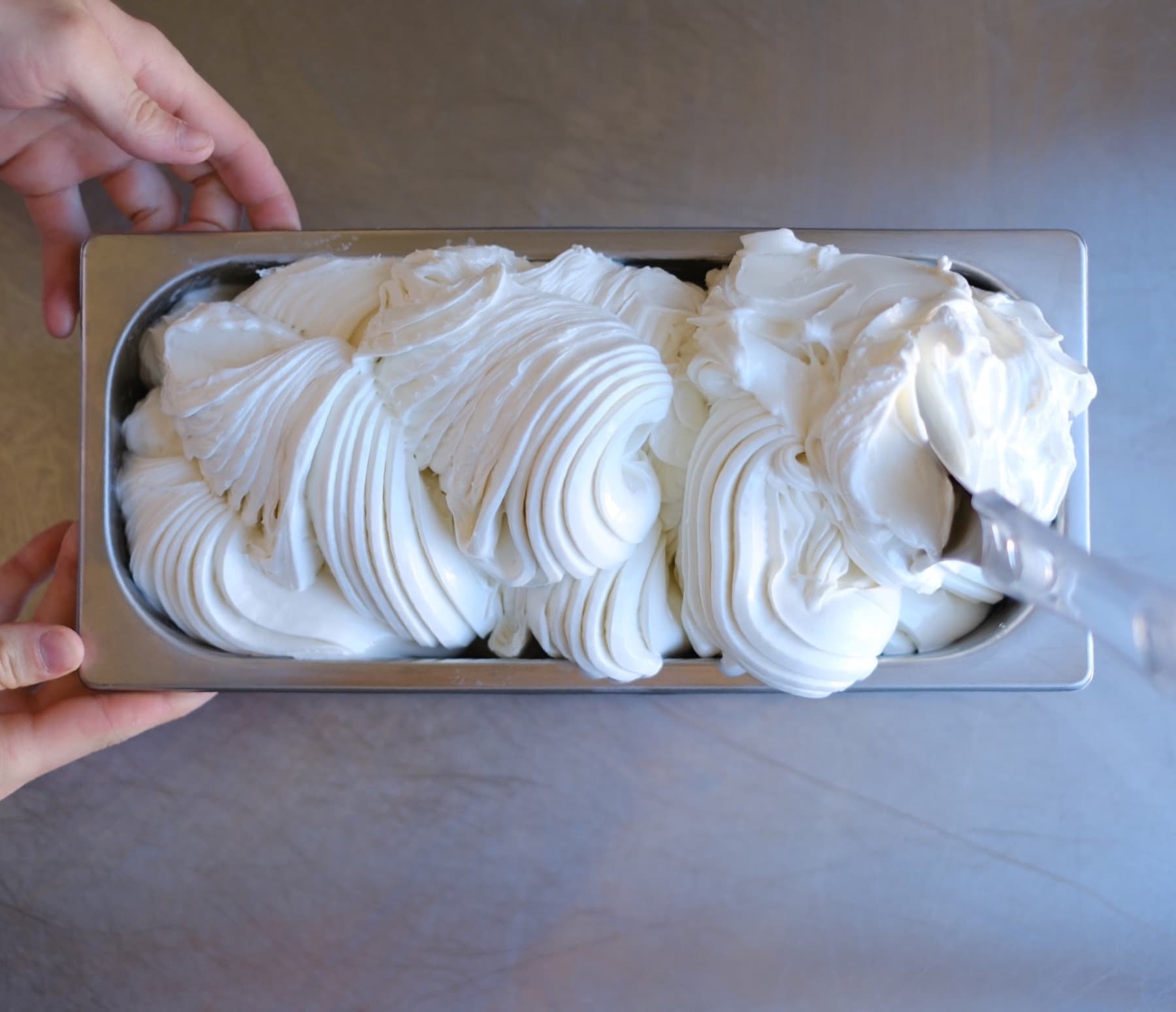 Nyproducerad gelato i en rostfri kantin med händer runt formen